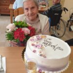 Starejša ženska s šopkom rož sedi ob torti.