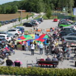 Več starejših ljudi in otrok izvaja telovadbo na prostem s pomočjo ponjave in žoge.