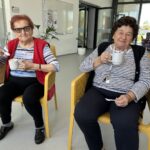 Dve starejši ženski sedita in v rokah držita skodelice.