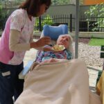 Ženska pomaga starejši ženski na invalidskem vozičku pri hranjenju.