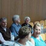 Skupina žensk sedi na stolih v dvorani.