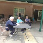 Tri starejše ženke sedijo na stolih pred stavbo.