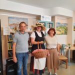 Moški in ženska stojita ob ženski s slamnatim klobukom in košaro v roki.