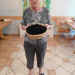Starejša ženska stoji in v rokah drži košaro s papirnatimi kroglicami.