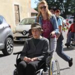 Ženska spremlja starejšo gospo na invalidskem vozičku.