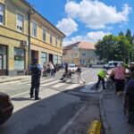 Več ljudi z invalidskimi vozički in spremljavalci prečka prehod za pešce.