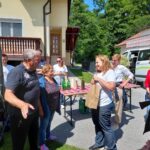 Starejši gospod na levi govori proti ženski na desni. Okoli njuju stoji več ljudi.