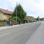 Daljša kolona ljudi, ki spremljajo starejše ljudi na vozičkih.