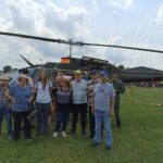 Več ljudi stoji pred vojaškim helikopterjem.
