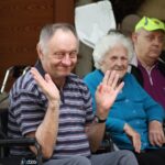 Dva starejša moška in ženska sedijo na invalidskih vozičkih.