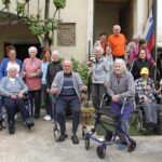 Več ljudi stoji oz. sedi na invalidskih vozičkih pred stavbo.