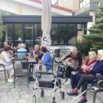 Več starejših ljudi sedi pred stavbo na kateri je napis "Domska kavarna".