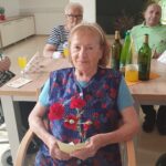 Starejša gospa sedi in v rokah drži rožico.