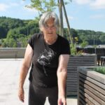 Starejša ženska stoji in v roki kaže sadove drevesa.