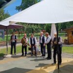 Skupina šestih starejših moških nastopa na prostem.