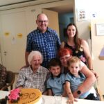 Več oseb ob mizi na kateri je torta z napisom "90".
