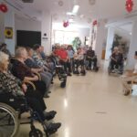 Več starejših oseb sedi v pokrogu in opazujejo žensko, ki sedi pred njimi.