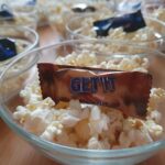 Steklene skodelice, napolnjene s pokovko, vsaka ima tudi zavitek čokolade z napisom "Get it". Skodelice so lepo postavljene na mizo, pripravljene za prigrizek ob gledanju filma.