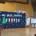 Oder, okrašen z baloni in ilustracijami otrok, z napisom 'Naš vrtec praznuje' pred začetkom prireditve.