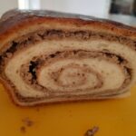Rezina orehove potice na rumeni deski. Vidi se spiralni vzorec testa in orehovega nadeva. Potica je lepo pečena, s svetlo zlatorjavo skorjo.