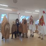 Skupinska fotografija več oseb v pustnih kostumih iz vrečevine in bele tkanine z barvitimi trakovi; na sredini stoji oseba v klobuku in predpasniku.