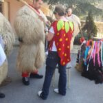 Bližnji posnetek dveh oseb v tradicionalnih kurent kostumih iz krzna. Ena nosi rdeč šal, druga pa je oblečena v kostum jagode. Videti sta, da se pripravljata na pustno praznovanje.