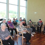 Stanovalci doma za starejše sedijo v skupini in spremljajo dogajanje, nekateri nosijo pionirske kape.