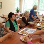 Skupina stanovalcev in sodelavk doma oblikuje kroglice iz zmesi za peko. Sestavine oblikujejo v kroglice in jih polagajo na pekače, obložene z aluminijasto folijo.