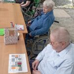 Starejše ženske in moški v invalidskih vozičkih sodelujejo pri igri tombole na terasi.