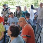 Udeleženci dogodka v kostumih stojijo v ozadju, v ospredju sedijo stanovalci doma, nekateri na invalidskih vozičkih.