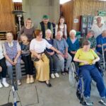 Skupinska fotografija stanovalcev doma in obiskovalcev v srednjeveških kostumih, posneta pod nadstreškom doma.