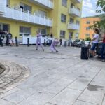 Dve deklici v vijoličnih trenirkah izvajata plesno točko na ploščadi pred domom, občinstvo in starši stojijo ob strani.