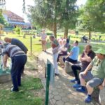 Stanovalci doma za starejše nastavljajo keglje med sproščenim druženjem na klopi v parku.