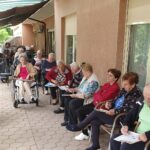 Skupina stanovalcev doma za starejše sedi pod nadstreškom in sodeluje v tomboli, vsak s kartončkom in svinčnikom v roki.