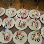 14 krožnikov s pripravljeno sladico banana split, okrašeno s smetano, čokoladnim prelivom, sladoledom in pisanimi dekoracijami.