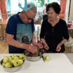 Starejši par pripravlja naribana jabolka v kuhinji doma starejših.