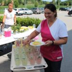 Zaposlena v domu pripravlja limonado na vozičku, okrašenem z rezinami limon in svežo meto.