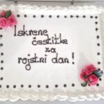 Sladka torta z belo smetano in napisom "Iskrene čestitke za rojstni dan!" z rožnatimi okrasnimi rožami.