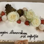Rojstnodnevna torta s posvetilom »Dragim stanovalcem vse najboljše«, okrašena z belimi vrtnicami, jagodami in makroni.