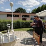 Dva starejša moška skupaj izvajata met pri ruskem kegljanju; eden pomaga drugemu usmeriti kroglo, nekaj kegljev je že podrtih.