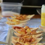 Na pladnju je več lesenih posodic z ocvrtim krompirjem, prelitem s kečapom in postreženim z majonezo.