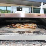 Pečena pizza v majhni zunanji peči, pogled od blizu na hrustljavo skorjo in stopljen sir.