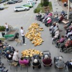 Stanovalci doma upokojencev v krogih na dvorišču, ob kupu razpolovljenih buč, spremljajo dogajanje.