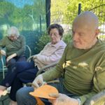 Stanovalec doma za starejše z oranžnim papirjem in škarjami ustvarja jesensko dekoracijo, ob njem sedita dve stanovalci.