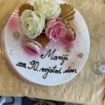 Torta z napisom »Mariji za 90. rojstni dan«, okrašena z rožami in makroni.