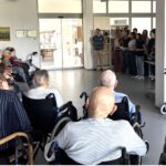 Stanovalci v vozičkih in na stolih sedijo v polkrogu, pred njimi stoji skupina mlajših ljudi z glasbenikom s kitaro, ki nastopajo.