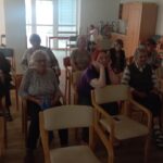 Stanovalci doma za starejše v zatemnjeni sobi sedijo na stolih in spremljajo projekcijo filma.