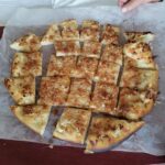 Pogled od zgoraj na pečen kruh z zapečeno skorjo, narezan na kvadratne kose, položen na peki papirju.
