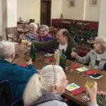 Skupina stanovalcev za mizo nazdravlja s kozarci, na mizi so nageljni in pijača.