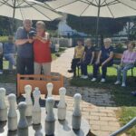 Par stanovalcev se v družbi gledalcev pripravlja na met s kroglo proti postavljenim kegljem.